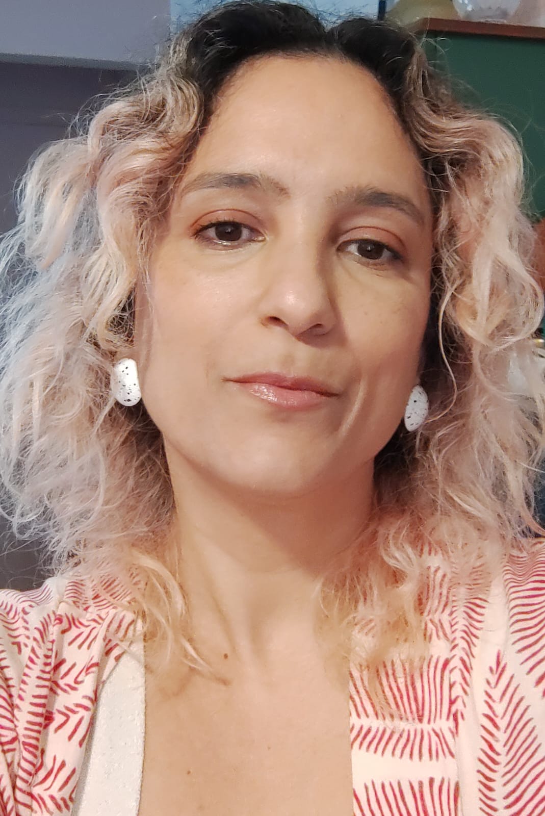 foto de rosto da roteirista Fabíola Alves, uma mulher de cabelos ondulados com as pontas rosas, usando uma blusa com tons rosa e vermelho fazendo um padrão floral abstrato